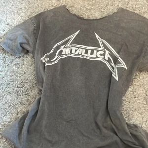 Grå Metallica t-shirt - Säljer en grå t-shirt med Metallica-logga i vitt. T-shirten har en vintage-look med korta ärmar och rund hals. Perfekt för alla rockälskare! 🤘