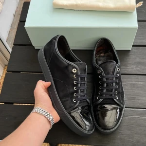 Lanvin skor  - Snygga  sneakers från Lanvin med glansiga detaljer på tån och snörning. Skorna har en stilren design med en kombination av olika material som ger en lyxig känsla. Perfekta för en trendig look. Vänster häl har en skada. Annars i bra skick! Uk 10. Box ingår. Går ner i pris vid snabb affär!