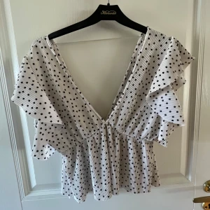 Vit prickig blus med volangärm - Supersöt vit blus med svarta prickar och djup v-ringning. Toppen har volangärmar och lätt rynkad midja. Toppen är i storlek M, men passar mig som vanligtvis har S❤️