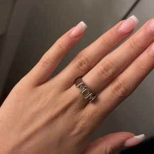 Silverring med texten MOM/WOW - Cool ring i silverfärg med stora bokstäver som stavar 'MOM' framtill. Upp och ner kan ringen också stavas ” WOW”  Ringen har en stilren och modern design, perfekt för att visa uppskattning till någon speciell. Passar både som statement piece eller som en personlig detalj i din smyckessamling.