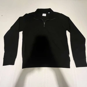 Svart half zip tröja Jack & Jones - Svart långärmad tröja från Jack & Jones med half zip-dragkedja vid halsen. Klassisk och stilren modell i mjuk bomull, perfekt för lager-på-lager. Ribbstickade muddar vid ärmslut och nederkant för en snygg passform. Org pris: 449kr.   Mitt pris 319kr men priset kan diskuteras.