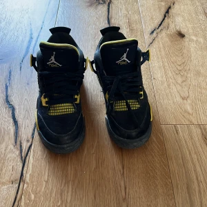 Nike Air Jordan 4 Retro Thunder svart/gul - Nike Air Jordan 4 Retro Thunder i svart och gul med coola meshdetaljer och klassisk Jumpman-logga på plösen. Skorna har snörning, vadderad plös och sula med synlig Air-enhet. Perfekt för dig som vill sticka ut med en ikonisk sneaker.
