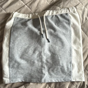 Grå och vit kortkjol med snörning - En fjol från hummel storlek 152. Sportig kortkjol i grått och vitt med breda sidor och elastisk midja. Kjolen har snörning framtill och är gjord i mjuk bomullsmix, perfekt för en chill och avslappnad look.liten fläck snöre, går säkert bort i tvätten. 
