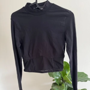 Svart croppad polotopp med meshdetalj - Säljer en svart croppad polotopp från NA-KD i storlek XS. Toppen har långa ärmar och en hög hals, samt en snygg meshdetalj nedtill som ger en cool touch. 