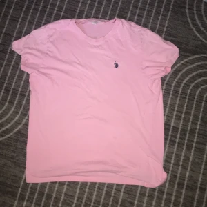 Rosa t-shirt från U.S. Polo Assn. - Snygg rosa t-shirt från U.S. Polo Assn. i storlek L. Klassisk modell med korta ärmar och rund halsringning. Liten broderad logga på bröstet. Skön och mjuk bomull som passar perfekt till jeans eller shorts.