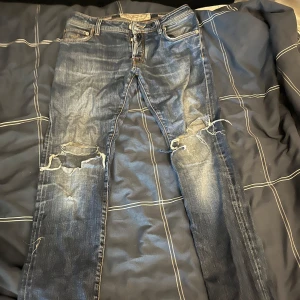 Blå slitna jeans från Jacob Cohen - Säljer ett par blå jeans från Jacob Cohen med coola slitningar och hål på båda benen. Klassisk femficksmodell med snygg tvätt och detaljer. Innerfodret har rutigt mönster. Perfekta för dig som gillar en avslappnad och trendig look. Priset är inte hugget i sten så priset kan diskuteras!!