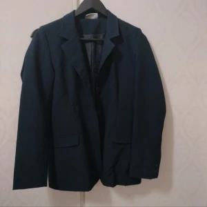 Mörkblå kavaj med klassisk passform - Snygg mörkblå kavaj med klassisk krage och två fickor framtill. Kavajen har knäppning framtill och är figursydd för en stilren look. Perfekt att styla med skjorta eller t-shirt för en clean outfit.