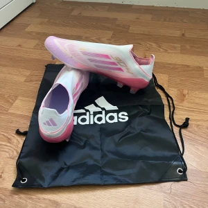 Lamine yamal fotbollskor F50 Elite  - Säljer ett par Adidas fotbollsskor i vitt och rosa med guldiga detaljer och genomskinlig sula. Skorna har en strömlinjeformad design utan snörning och är tillverkade i syntetmaterial. Perfekta för dig som vill sticka ut på planen med stilrena och sportiga skor. Elite Lamine yamal fotbollsskor säljer dem då de var fel storlek och gick inte att lämna tbx. Är använda ett par matcher men är som nya utan några problem.Priset går och diskuteras ställ frågor om ni undrar något😁.ingen ångresrätt!
