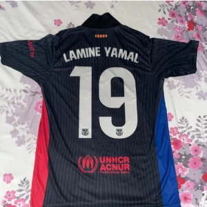 FC Barcelona Lamine Yamal tröja Nike M - Säljer en svart FC Barcelona fotbollströja med Lamine Yamal och nummer 19 på ryggen. Tröjan har röda och blå sidopaneler, klubbmärke och Nike-logga framtill samt Spotify och UNHCR-tryck. Tillverkad i Dri-FIT-material för bästa komfort.