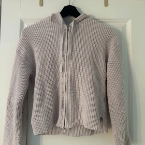 Ljusrosa stickad hoodie från Monki - Supermysig ljusrosa stickad hoodie från Monki i storlek XXS. Tröjan har dragkedja framtill, huva med snörning och långa ärmar. Perfekt för lager-på-lager och chill dagar. Snygg ribbad struktur och enkel att matcha med jeans eller kjol.