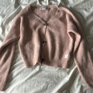 Rosa kofta från 157 med knappar - Mysig ljusrosa kofta från 157 med v-ringning och knappar framtill. Koftan är stickad och har långa ärmar, perfekt för lager på lager. Enkel och stilren modell som passar till det mesta.