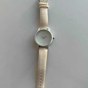 Vit klocka - Superfin vit klocka med stilrent klockur och armband i konstläder. Batterier behöver bytas då den legat i skrivbordslådan ett tag. Om man tycker det är viktigt att den visar tiden, det vill säga.   Hämtas i Stockholm eller skickas mot porto.  Kolla gärna mina andra annonser också!