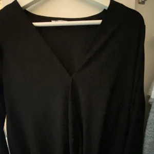 Svart klänning med v-ringning - En stilren svart klänning med djup v-ringning. Perfekt för dig som gillar minimalistiskt mode och vill ha en klassisk look.