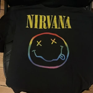 Nirvana t-shirts med smileytryck - Två coola Nirvana t-shirts med det klassiska smileytrycket på ryggen. En svart med regnbågsfärgat tryck och en gul med svart tryck. Perfekta för dig som gillar bandmerch och vill sticka ut. Båda är kortärmade och i mjuk bomull. Säljer dem ihop för 200kr annars 120kr st