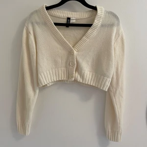 Vit croppad kofta - Superfin croppad kofta i vit från H&M . Tröjan har v-ringning, ribbade muddar och knappar framtill. Perfekt att slänga över ett linne eller klänning. Långärmad och stickad i mjukt material för en chill vibe. Knappt använd. Psst vid köp av varan kommer du få ett litet sticker! xx 