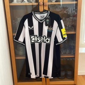 Newcastle United hemmatröja 2023-2024 Castore M - Snygg Newcastle United hemmatröja från Castore i storlek M. Klassisk svartvit randig design med klubbmärke och sponsortryck på bröstet samt gul detalj på ärmen. Tillverkad i lätt och ventilerande polyester, perfekt för match eller träning. Samlar själv på fotbollströjor och kan garantera att varan är 100% äkta!