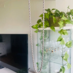 Silverfärgat tvinnat halsband - Snyggt halsband i silverfärg med tvinnad kedja som ger en cool och stilren look. Kedjan har en klassisk karbinhake och passar perfekt för att lyfta din outfit. Perfekt accessoar för dig som gillar minimalistisk men ändå iögonfallande stil. Halsbandet är 4mm brett och 50 cm långt.
