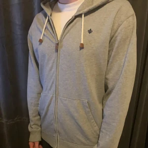 Grå hoodie med dragkedja från Morris - Snygg ljusgrå hoodie från Morris med dragkedja, huva och vita snören med bruna detaljer. Pris kan diskuteras vid snabba affärer