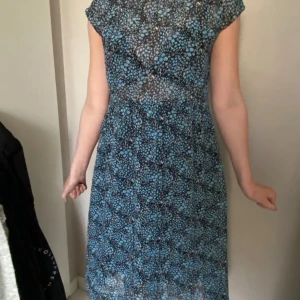 Blåmönstrad klänning med korta ärmar - Säljer en blå och svart klänning med småblommigt mönster. Klänningen har korta ärmar, rund halsringning och en normal passform. Perfekt för vår och sommar. Längden går till knäna och materialet känns lätt och luftigt.