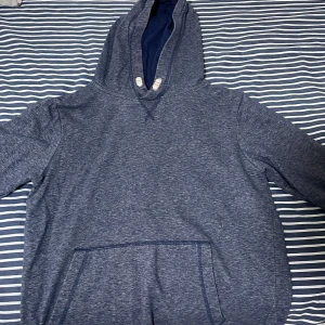 Blå hoodie från H&M - Mysig blå hoodie från H&M med känguruficka och justerbar huva. Tröjan har långa ärmar och ribbade muddar vid ärmslut och nederkant. Perfekt för en avslappnad stil.