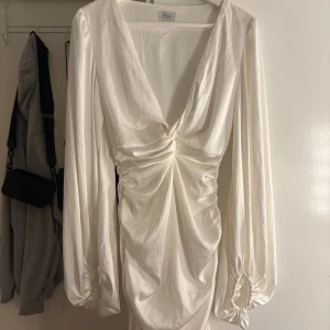 Vit omlottklänning från Oh Polly - Vit kortklänning från Oh Polly med djup v-ringning och långa puffärmar. Klänningen har omlottdetalj och rynkningar framtill. Använd någon gång bara men är i väldigt fint skick. 