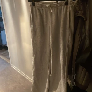 Gråa mjukisbyxor med dragsko - Säljer ett par gråa mjukisbyxor med resår och dragsko i midjan. Byxorna har en rak och loose passform, perfekta för en avslappnad stil. Tillverkade i mjukt bomullsmaterial för extra komfort.