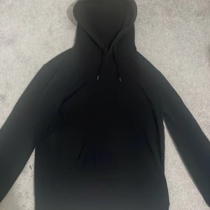 Svart hoodie från H&M - Säljer en svart hoodie från H&M i relaxed fit. Tröjan har huva med dragsko och långa ärmar. Perfekt för en avslappnad stil och enkel att matcha med det mesta.