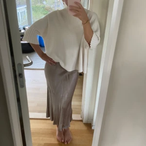 Beige långkjol i satin - Säljer en beige/guldig långkjol i glansigt satinmaterial. Kjolen har en figurnära passform upptill och faller snyggt längs benen med lätt utsvängd nederdel. Perfekt att styla med en stickad tröja eller en enkel topp.