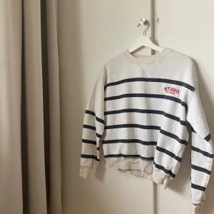 Vit och svart randig sweatshirt  - Vit sweatshirt med svarta horisontella ränder och liten röd Studio-logga på bröstet. Tröjan har rund halsringning, långa ärmar och ribbade muddar vid ärmslut och nederkant. Perfekt för en avslappnad stil. Pris diskuteras💘