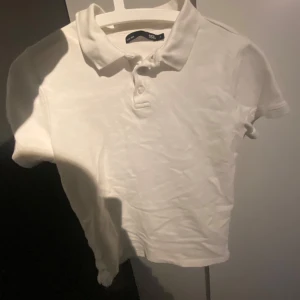 Vit piké t-shirt från 157 - Klassisk vit piké t-shirt från 157 med krage och knappar framtill. T-shirten har korta ärmar och är tillverkad i ett bomullsliknande material. Perfekt för en clean och enkel stil.