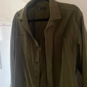 Olivgrön overshirt från C - Säljer en olivgrön overshirt från C i storlek S. Skjortan har klassisk krage, knäppning framtill och två bröstfickor. Perfekt att bära som lager över en t-shirt eller tröja.
