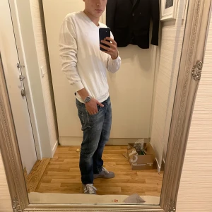 Vit långärmad tröja med v-ringning Tiger of sweden - Säljer en stilren vit långärmad tröja med v-ringad hals. Tröjan har en klassisk passform och är perfekt att matcha med jeans eller andra byxor. Enkel och tidlös design som funkar till många tillfällen. Denna är för stor för mig som man möjligtvis kan se. Står XL men minskat i tvätten