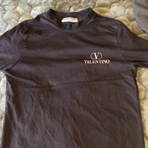 Svart t-shirt från Valentino - Svart äkta t-shirt från Valentino med logga tryckt på bröstet och stor VALENTINO-text längs nedre delen av ryggen. Klassisk rund hals och korta ärmar. Perfekt för dig som gillar stilrena designer och exklusiva märken! QR kod går att skanna🤑🤑Perfwkt under en tröja så man ser texten vid ryggen