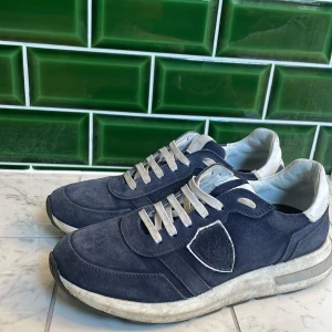 Blå Philippe model haute  - Säljer ett par blå Philippe Model sneakers med vita detaljer och grå snörning. Skorna har en klassisk sneakerdesign med rund tå och platt sula. Ovandelen är i mocka och syntet, och insidan är mjukt fodrad för extra komfort. (Smutsiga just nu enkelt att skrubba bort.) Går att förhandla med priset.