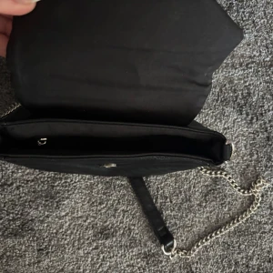 Svart quiltad axelväska med kedja - Jag Säljer en svart quiltad axelväska med silverfärgad kedjerem och justerbar axelrem i syntet. Väskan har ett stilrent mönster och stängs med lock. Perfekt för att bära det viktigaste. Och väldigt fin att ha tex till skolavslutningen 💕