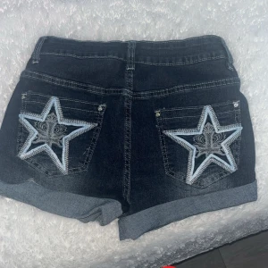 Mörkblå jeansshorts med stjärndetalj - FINNS OCKSÅ I M!!! Snygga mörkblå jeansshorts med uppvikta ben och stora broderade stjärnor i vitt och ljusblått på bakfickorna. Perfekta för en cool och avslappnad stil.❤️