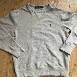 Ralph Lauren sweatshirt - Klassisk grå sweatshirt från Polo Ralph Lauren med broderad marinblå logga på bröstet. Tröjan har rund halsringning och långa ärmar. Tillverkad i en mjuk bomullsblandning för extra komfort. Öppen för alla frågor👍