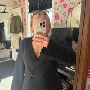 Svart stickad kofta  - Säljer en svart kofta i ullblandning från neo noir. Koftan har en enkel, stilren design med v-ringning och en knapp framtill. Långärmad och passar perfekt för kyligare dagar. Snygg och tidlös modell.