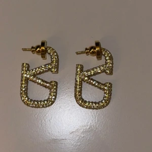 Glittriga örhängen i guld - Säljer ett par snygga örhängen i guld med glittrande stenar. De har en unik, geometrisk form och är perfekta för att ge din outfit lite extra bling.