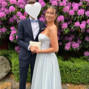 Ljusblå axelbandslös balklänning med pärlor och snörning - Säljer min ljusblå axelbandslös balklänning med pärldetaljer upptill både fram och bak, och snörning i sidan. Snörningen gör det enkelt att justera passformen så den sitter precis som du vill ha den. Klänningen har en vacker, flowy kjol och markerad midja. Perfekt balklänning enligt mig!