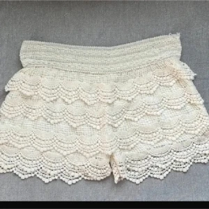 Vita virkade shorts med spetsdetaljer - På 3 vilken är de nedvikta, vilket inte alls behövs!Säljer ett par vita virkade shorts med bred resår i midjan och fina spetsdetaljer i lager på lager. Perfekta för varma dagar och ger en romantisk känsla till outfiten. S-m