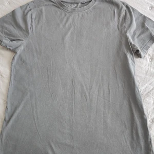 Grå t-shirt från Next - Säljer en enkel och stilren grå t-shirt från Next i 100% bomull. T-shirten har rund halsringning och korta ärmar, perfekt för en avslappnad look.