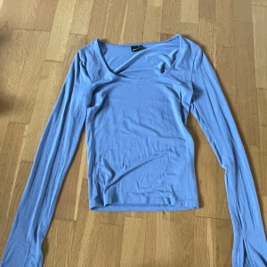 Ljusblå långärmad topp från Gina Tricot - Säljer en ljusblå långärmad topp från Gina Tricot. Toppen har en djup, rundad ringning och är figurnära i modellen. Perfekt att styla med jeans eller kjol för en enkel och snygg look.