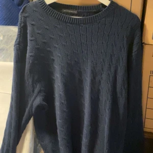 Mörkblå kabelstickad tröja - Mörkblå kabelstickad tröja  med rund halsringning och långa ärmar. Klassisk och stilren design med strukturstickat mönster. Perfekt för lager-på-lager under kyligare dagar.