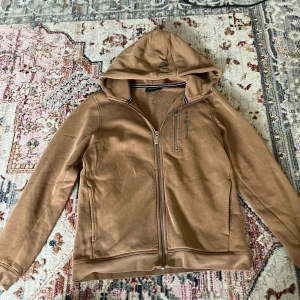 Beige hoodie från Sail Racing - Säljer en beige hoodie från Sail Racing med dragkedja framtill och huva. Jackan har en bröstficka med dragkedja och mjukt foder på insidan. Perfekt för kyliga dagar och enkel att matcha med det mesta. Den är köpt för 879kr från kidsbrandstore. Den är storlek 150.