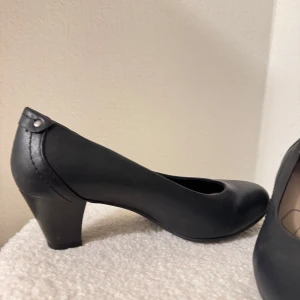 Svarta pumps låg klack - Säljer ett par klassiska svarta pumps med rund tå och låg klack. Skorna har en stilren design i syntetiskt läder med en matt finish och passar perfekt till dig som vill ha en enkel och tidlös sko till många tillfällen.