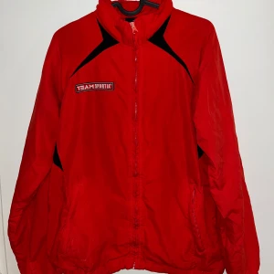 Röd sportig vindjacka  - En snygg vindjacka från Team Sportia som har dragkedja framtill, hög krage, två fickor och  storleken XS som passar både (34/36). Flowy och skön! 🏓