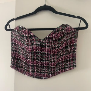 Rutig tubtopp i tweed - Säljer en snygg bandeau topp / korsett i tweed med rutigt mönster i rosa, svart, vitt och grönt. Toppen har en hjärtformad urringning och är något croppad. Från Zara och endast använd 1 gång 
