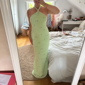 Ljusgrön långklänning med blommigt mönster - Säljer en ljusgrön långklänning med små lila blommor från Adoore. Klänningen har halterneck med knäppning i nacken, slits på sidan och figurnära passform. Aldrig använd, saknas dock prislapp. Storlek 38. 