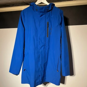 Blå Gore-Tex jacka från Sail Racing - Blå Sail Racing Goretex regnjacka/poncho med huva i storlek S. Jackan har två dragkedjor framtill (en vanlig och en för link technology) samt knappar. Jackan har används sparsamt under några få golfrundor men söker nu en annan. Utmärkt skick förutom ett pyttelitet märke på insidan som inte påverkar funktionen. Kostar 4000kr nypris. Hör gärna av dig vid frågor!